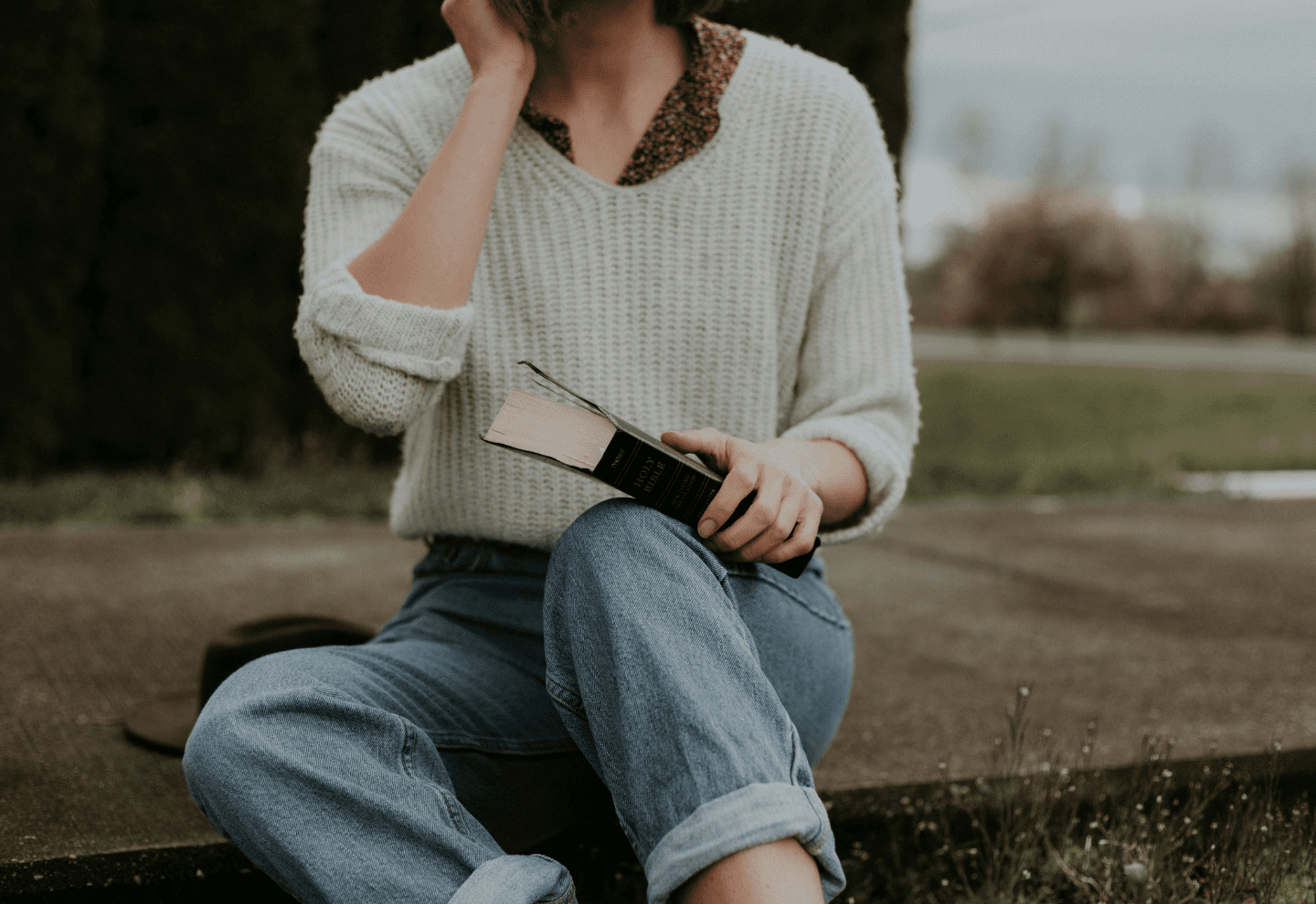 A woman sitting on the ground while holding a book.