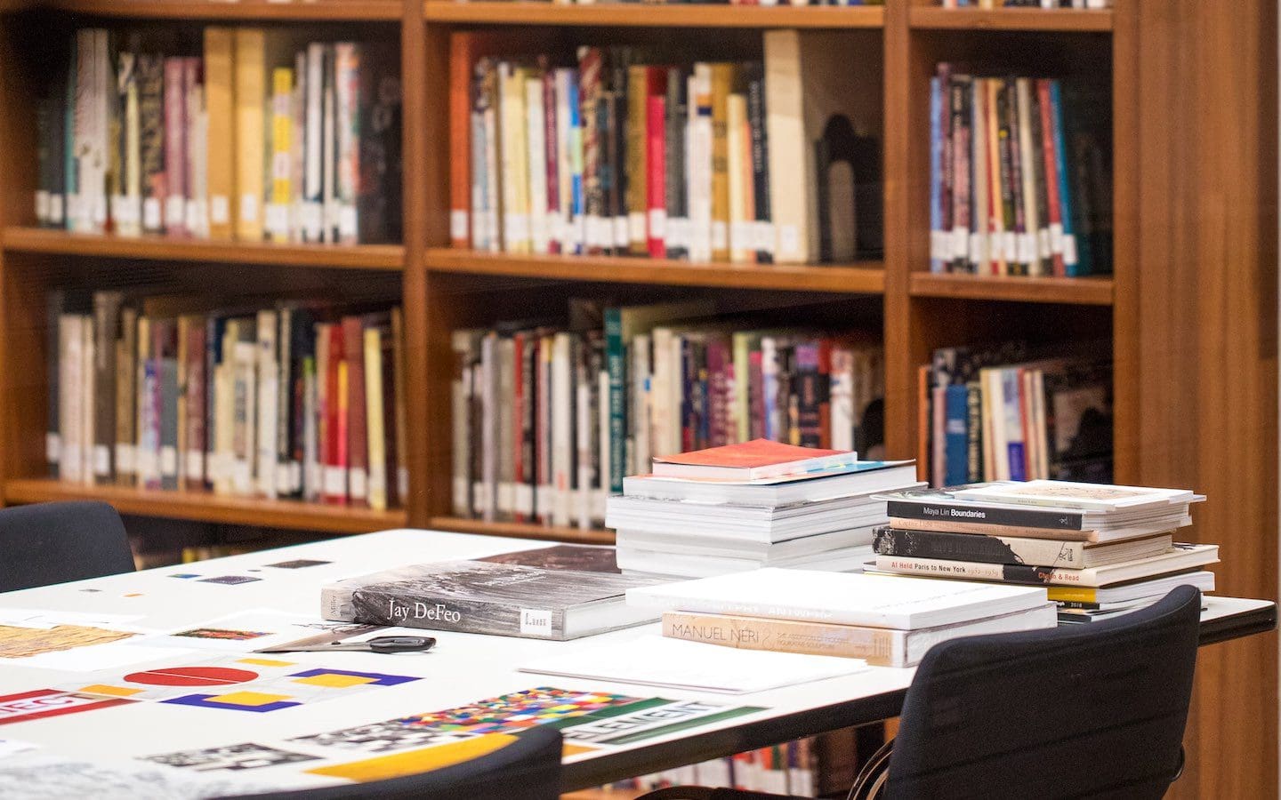The interior of a public school library with books sitting on a table in the foreground and a shelf of books in the background.