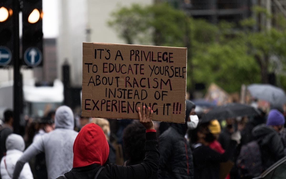 A person during a protest holding a cardboard sign that says