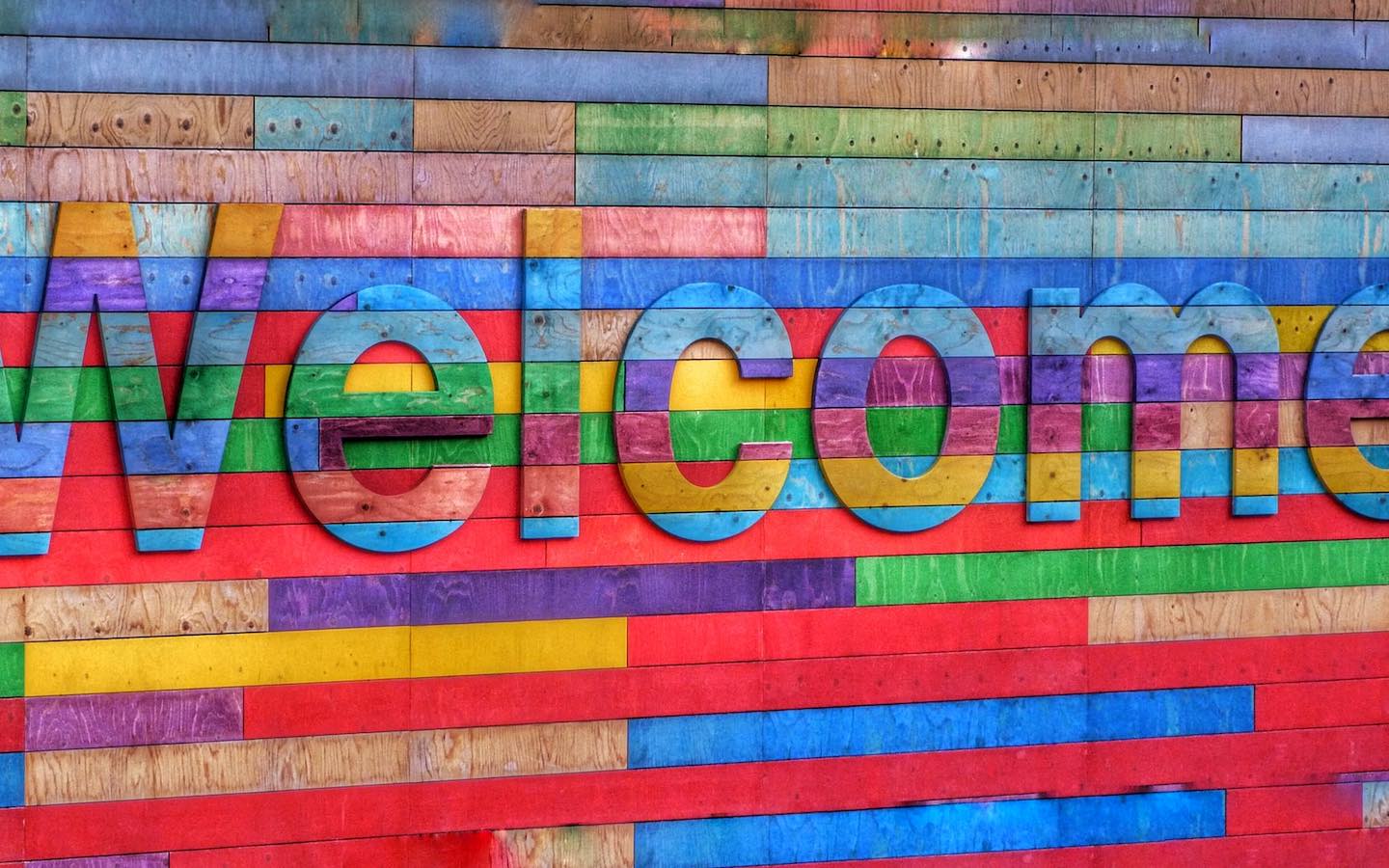 A wall of rainbow-colored wood pieces with the word “Welcome” across it.