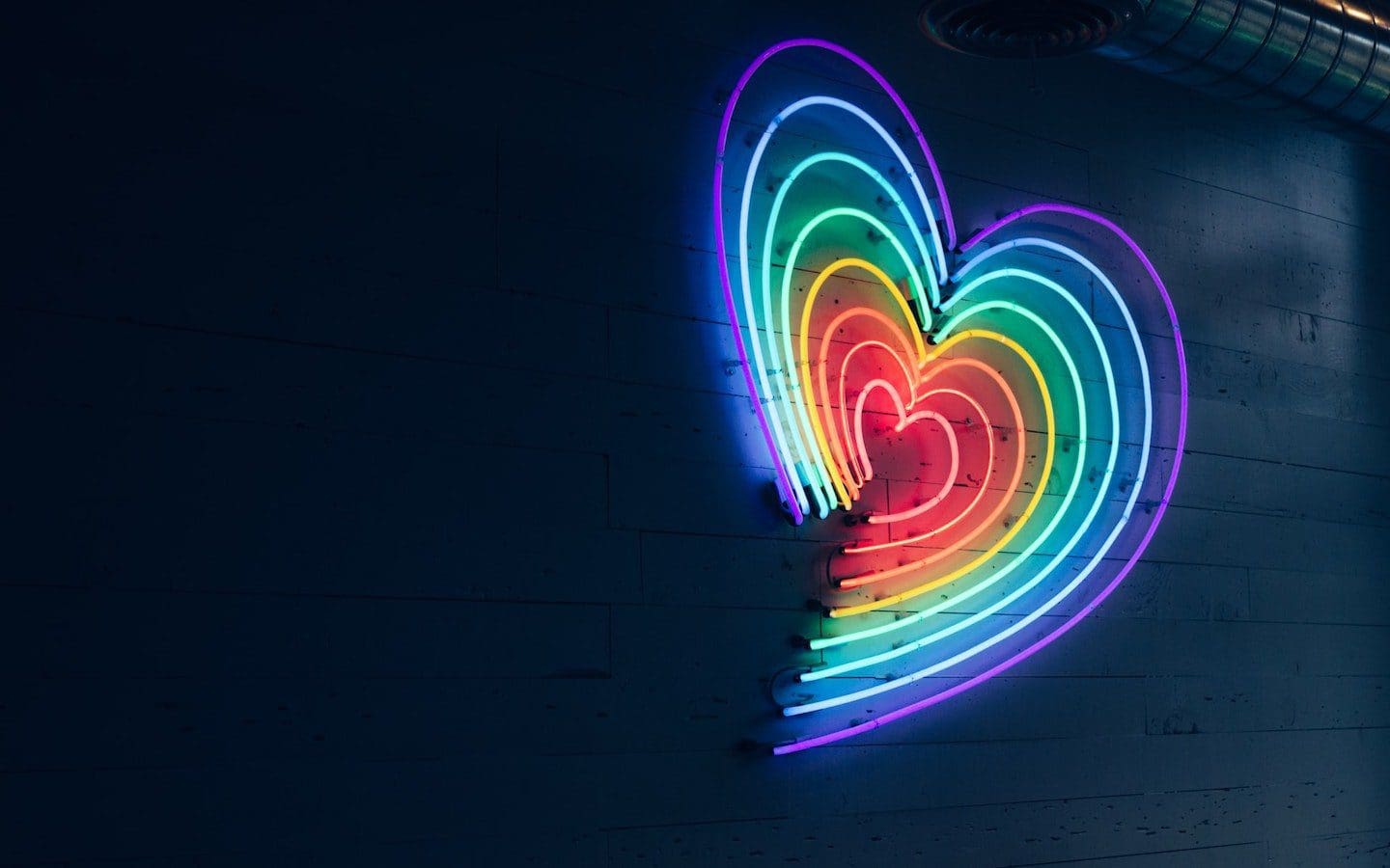 A neon light in the shape of a heart with rainbow colors.