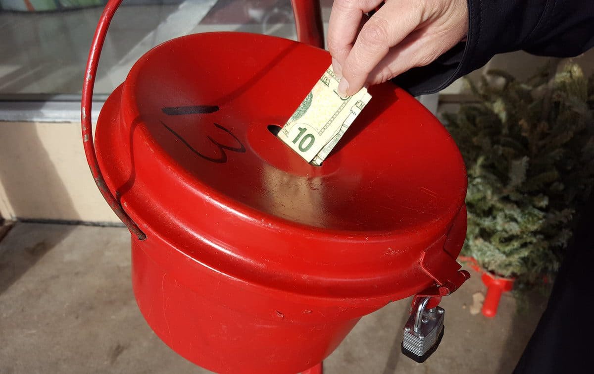 A red Salvation Army donation kettle with someone placing a $10 bill inside.