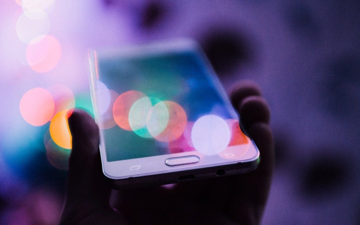 A person holding a smartphone with colorful circles of light around the device.