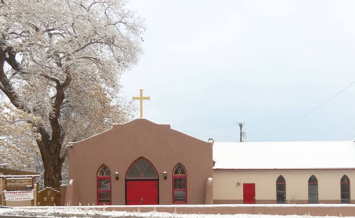 The exterior of a church in the winter with snow on the roof.