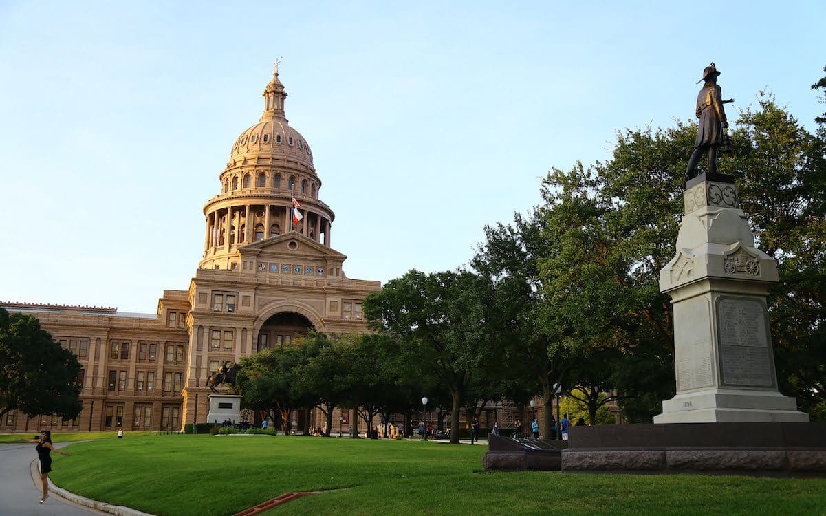 The front of the Texas Capitol building with trees lining the sidewalk.
