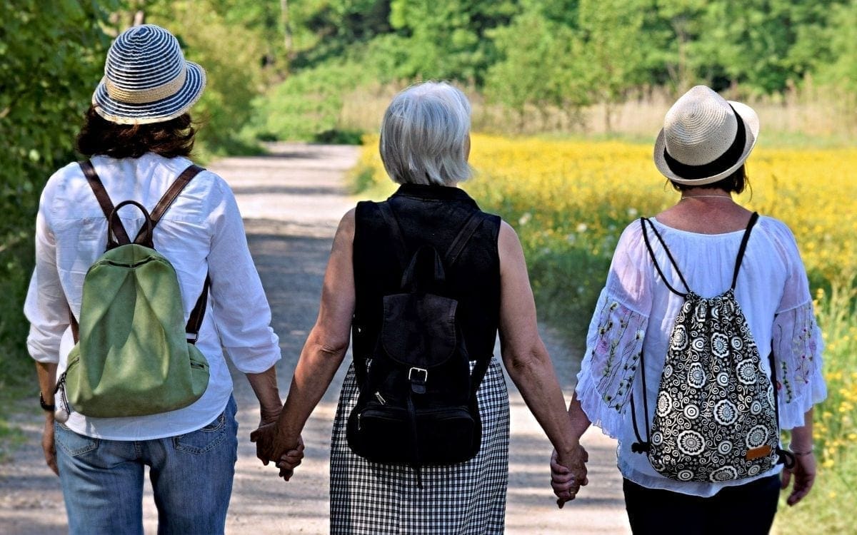 Three women friends holding hands as they walk down a road