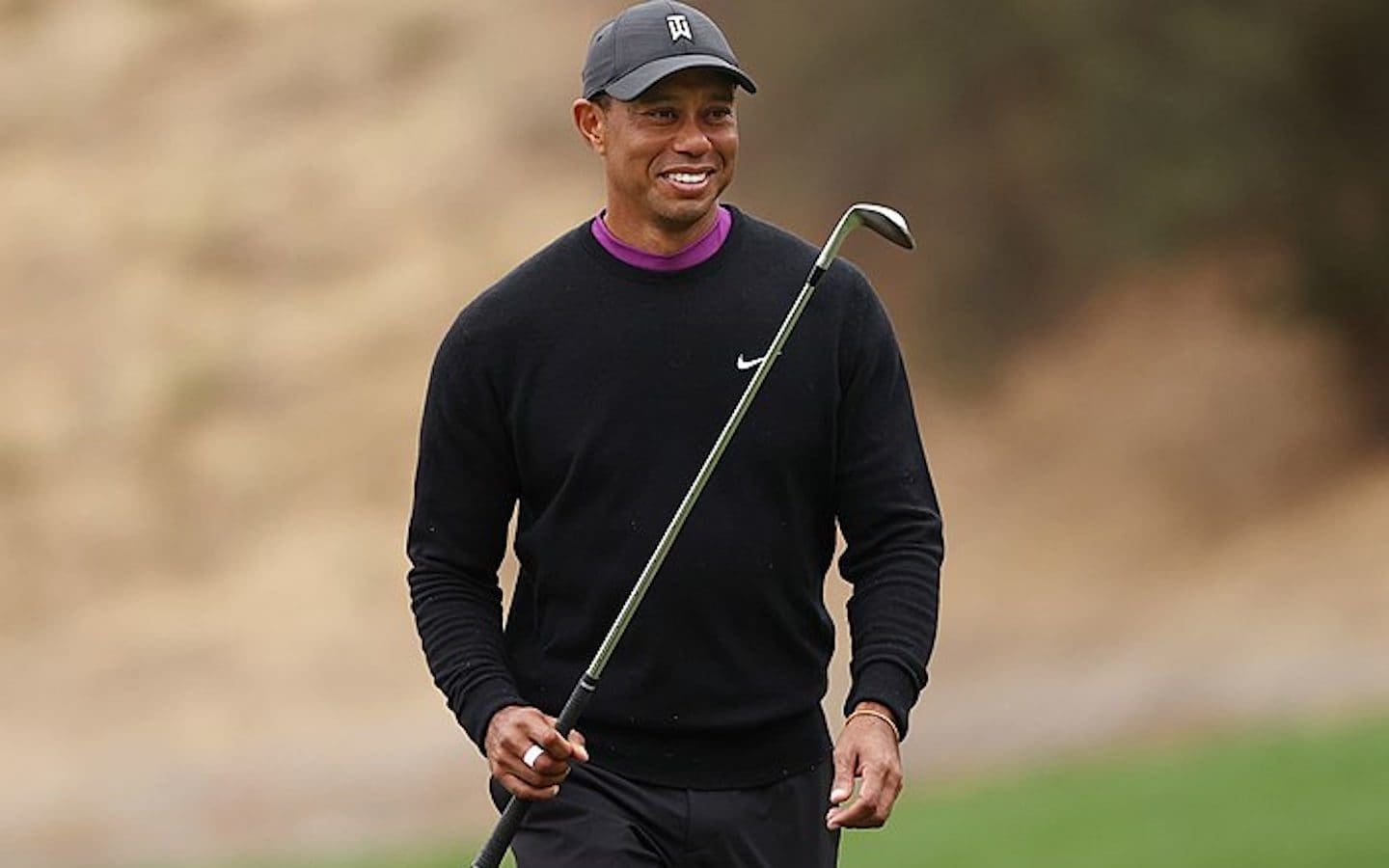 Tiger Woods holding a golf club and smiling.