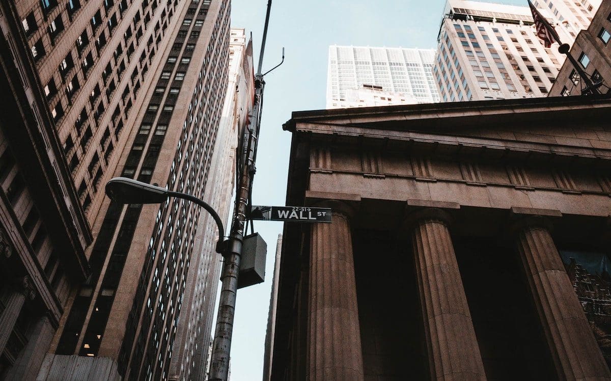 A sign for Wall Street in New York City seen from below with buildings in the background.