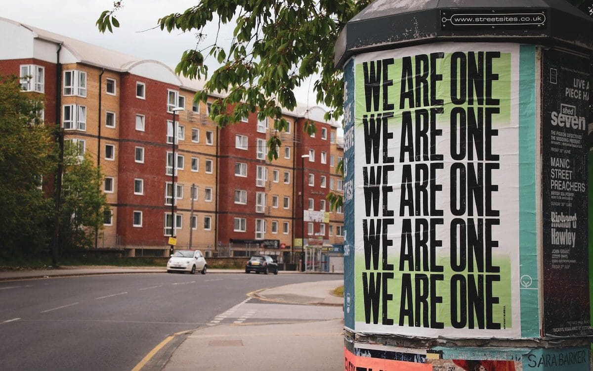 A street scene with a sign on a post that has “We Are One” on it multiple times.