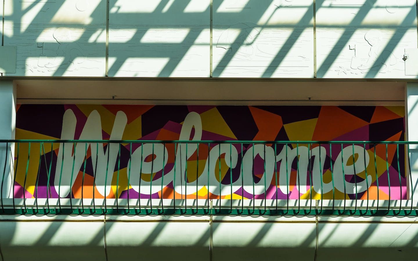 A wall with the word “welcome” painted on it in white letters with color patches surrounding it.