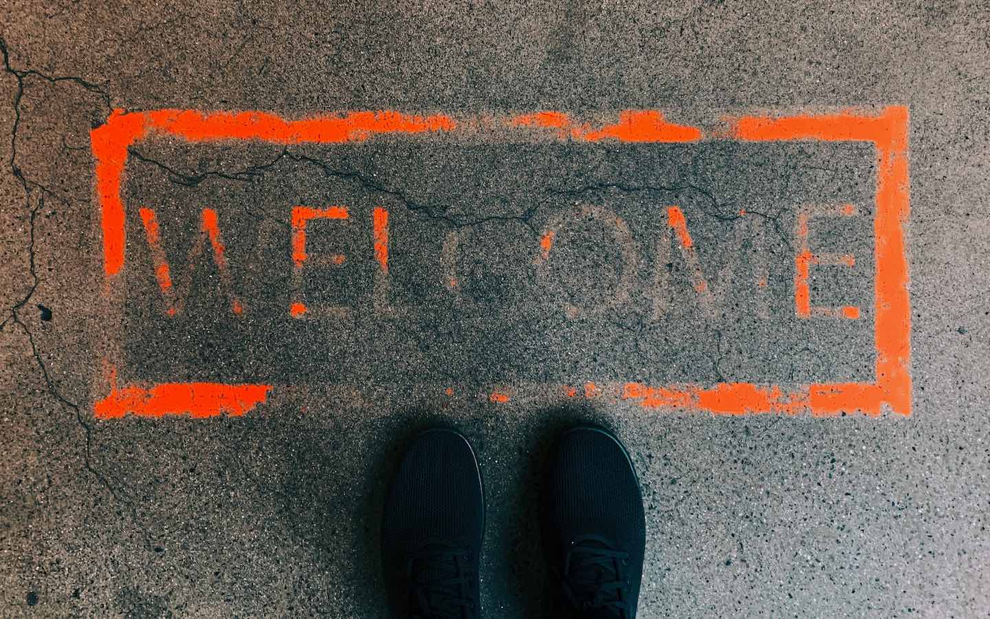 A red sign painted on concrete with the word “welcome” faded.
