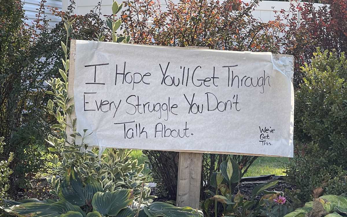 A sign in a flower bed offering a word of encouragement to passersby.|A sign in a flower bed offering a word of encouragement to passersby.|Two women praying together with their hands on each other's shoulders.