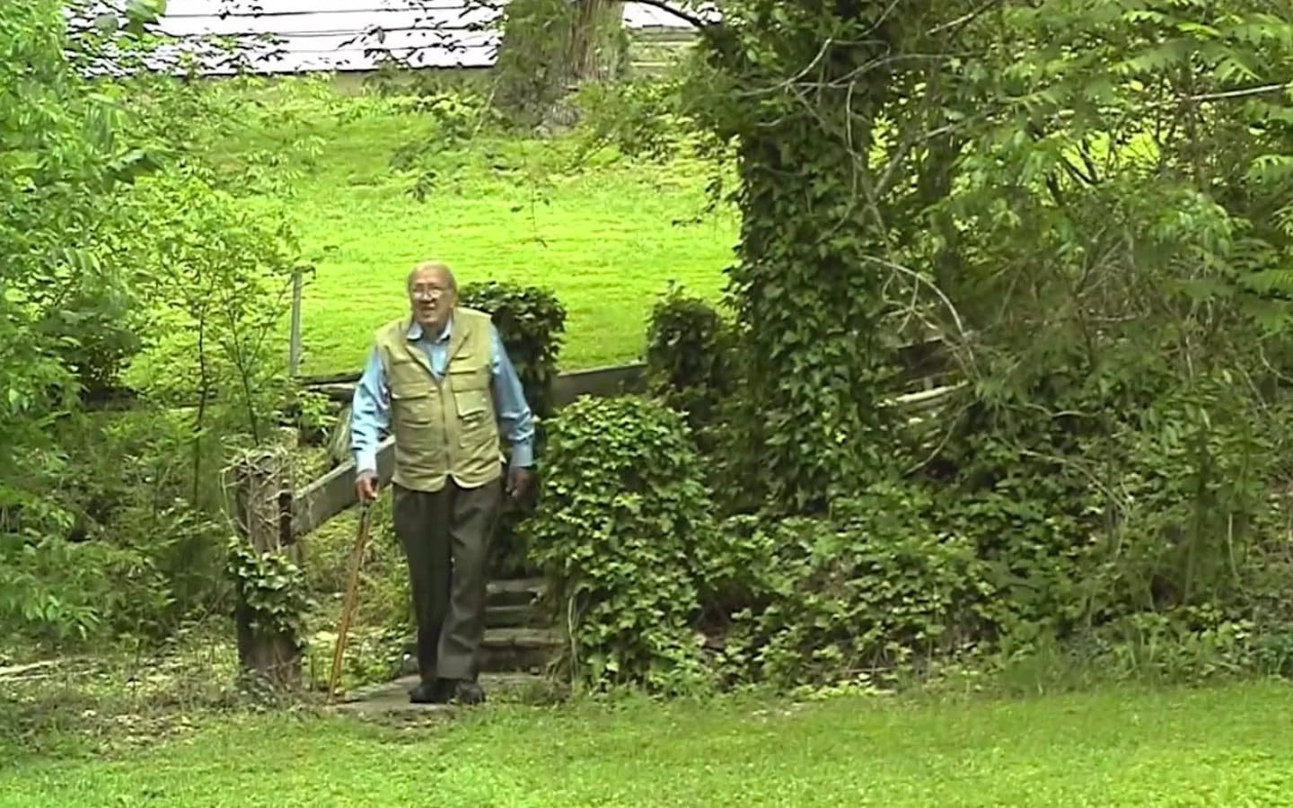 A man walking through a grassy field with a walking stick.