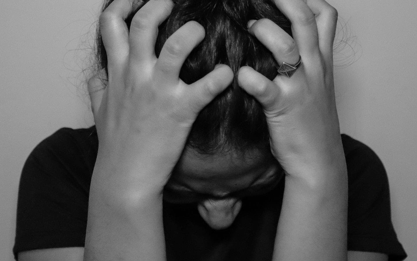 A woman with her head bowed and her hands on her head