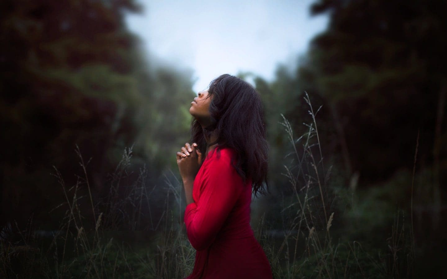 A woman standing outside in a field with her hands clasped together