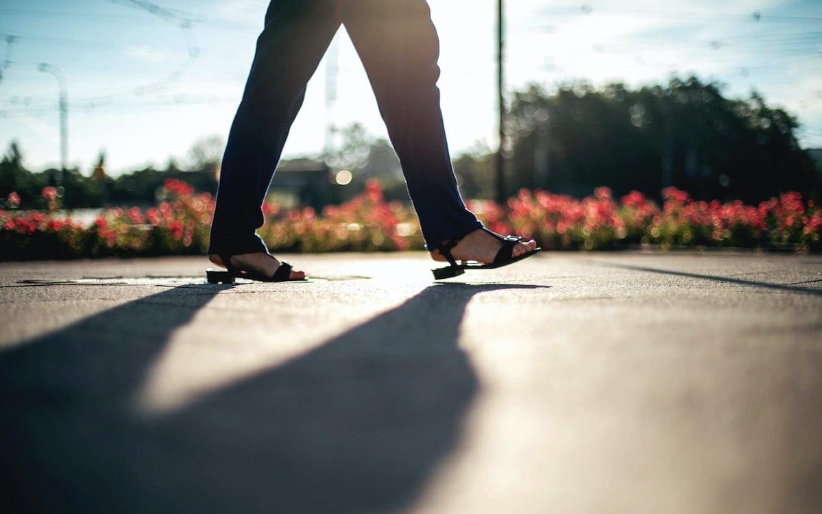 A woman walking down a sidewalk with only the lower half of her legs shown.