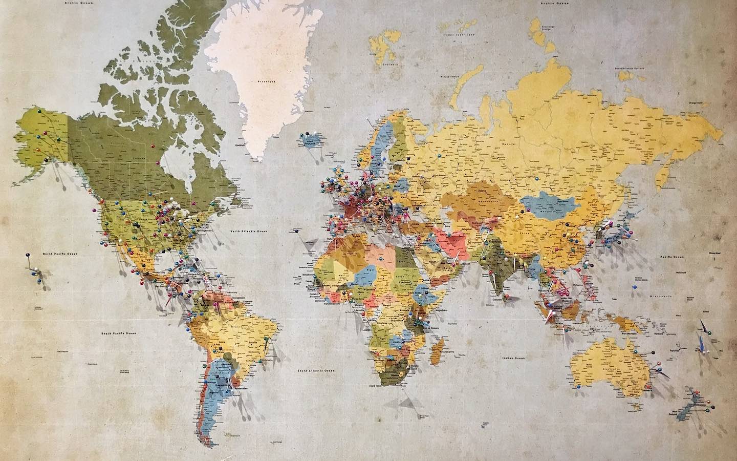 A world map displayed on a wall with pins in various locations.