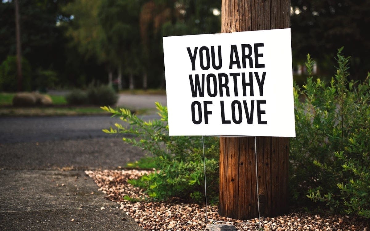 A white sign with black letters on a roadside that says