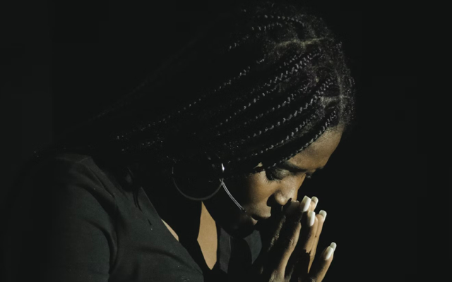 A woman dressed in black with her hands clasped and her head bowed.