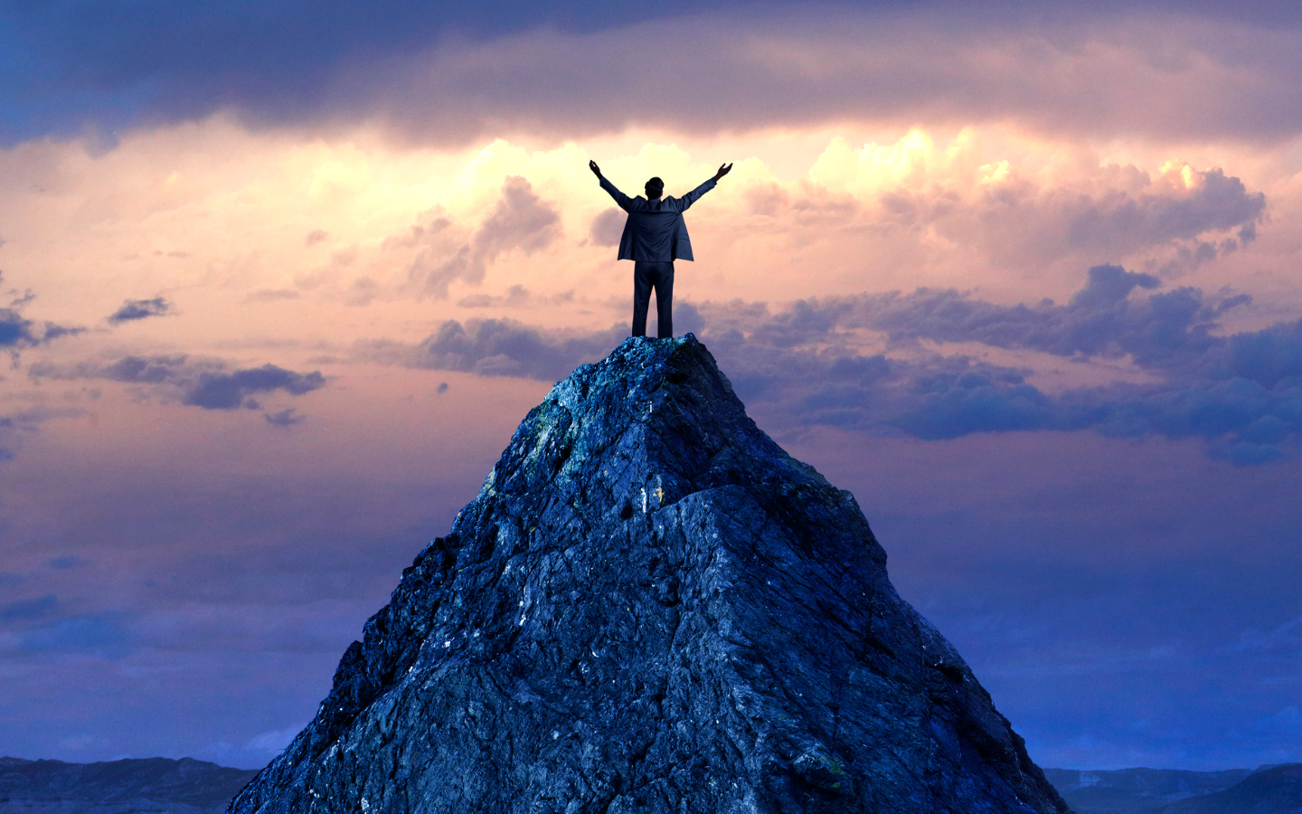 A man in a suit on top of a mountain summit.