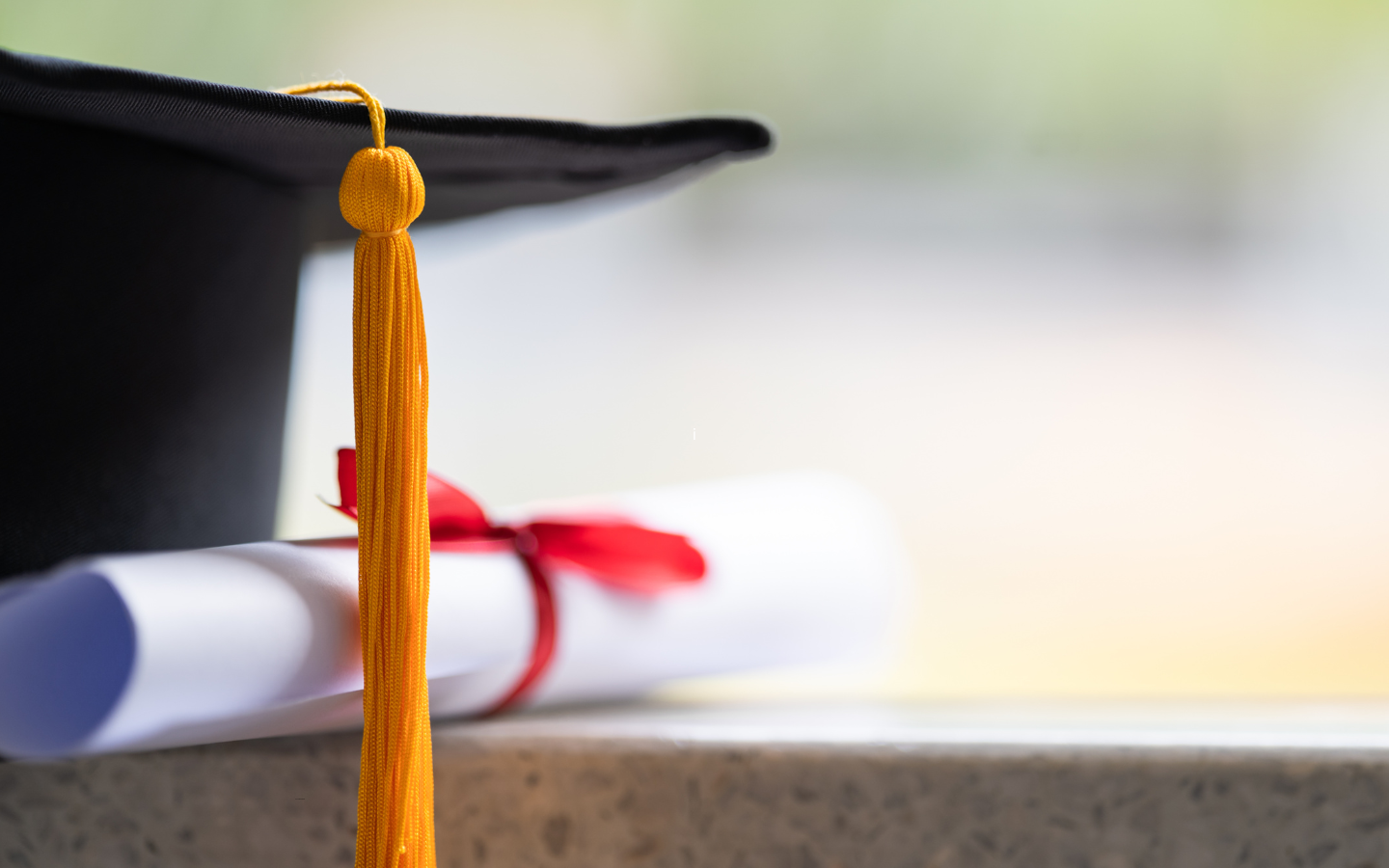 A photo of a graduation cap next to a rolled up diploma.