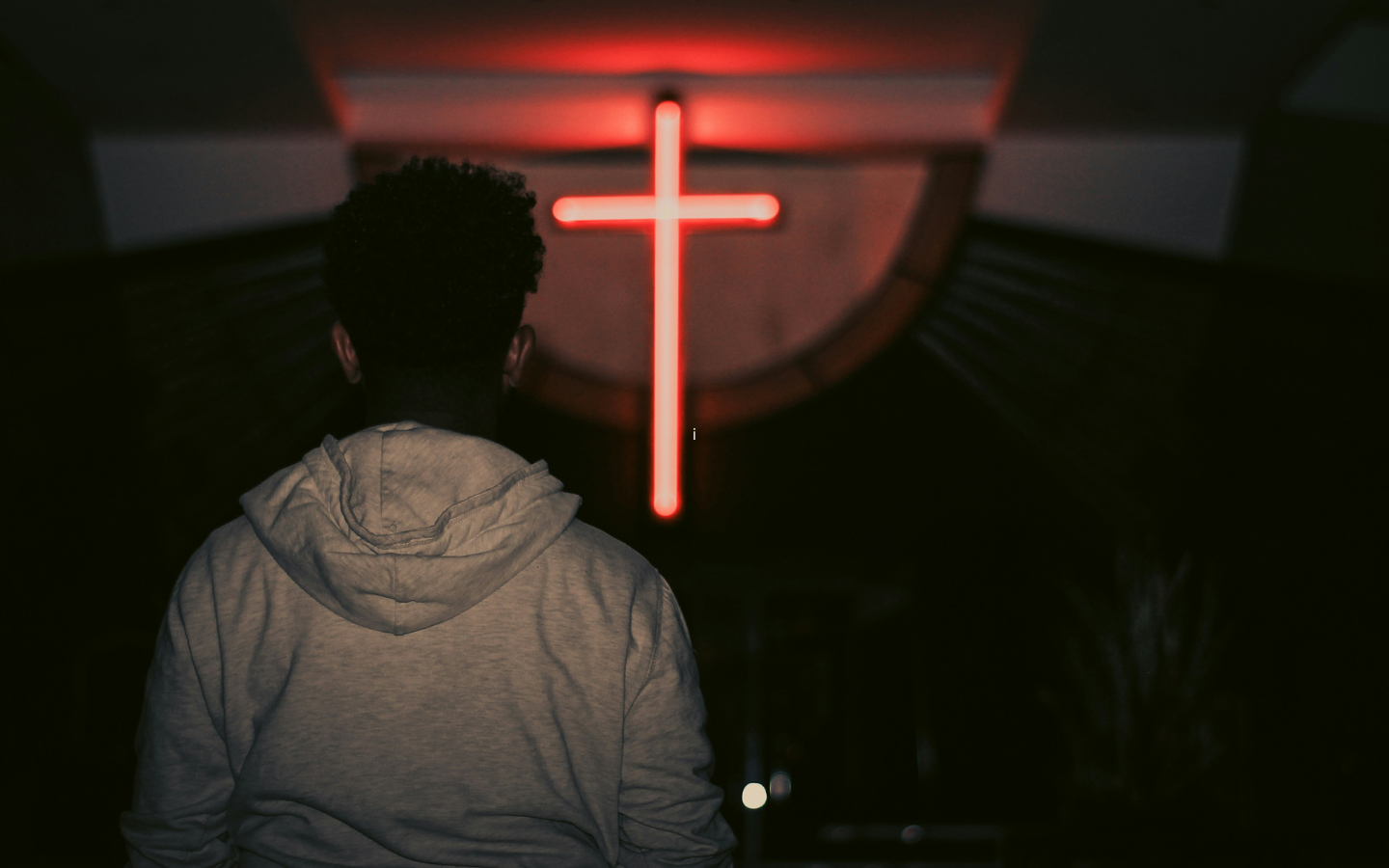 A person standing before a neon cross.