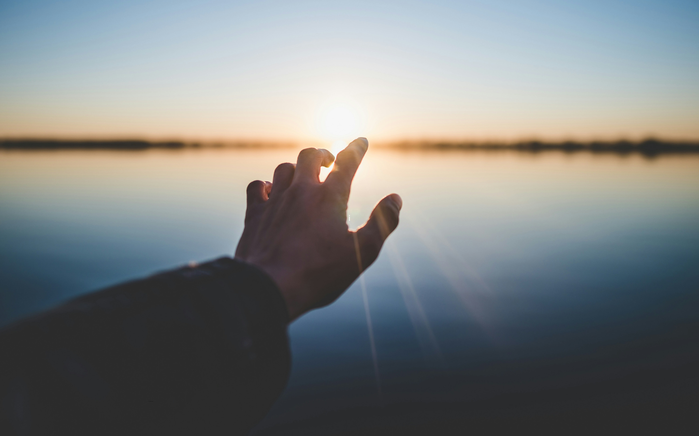 A hand stretched out in hope toward a sunrise.