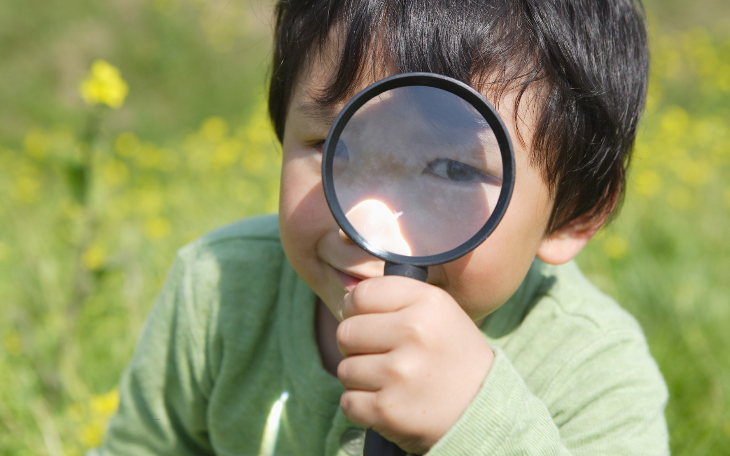 A young child explores nature with a magnifying glass.