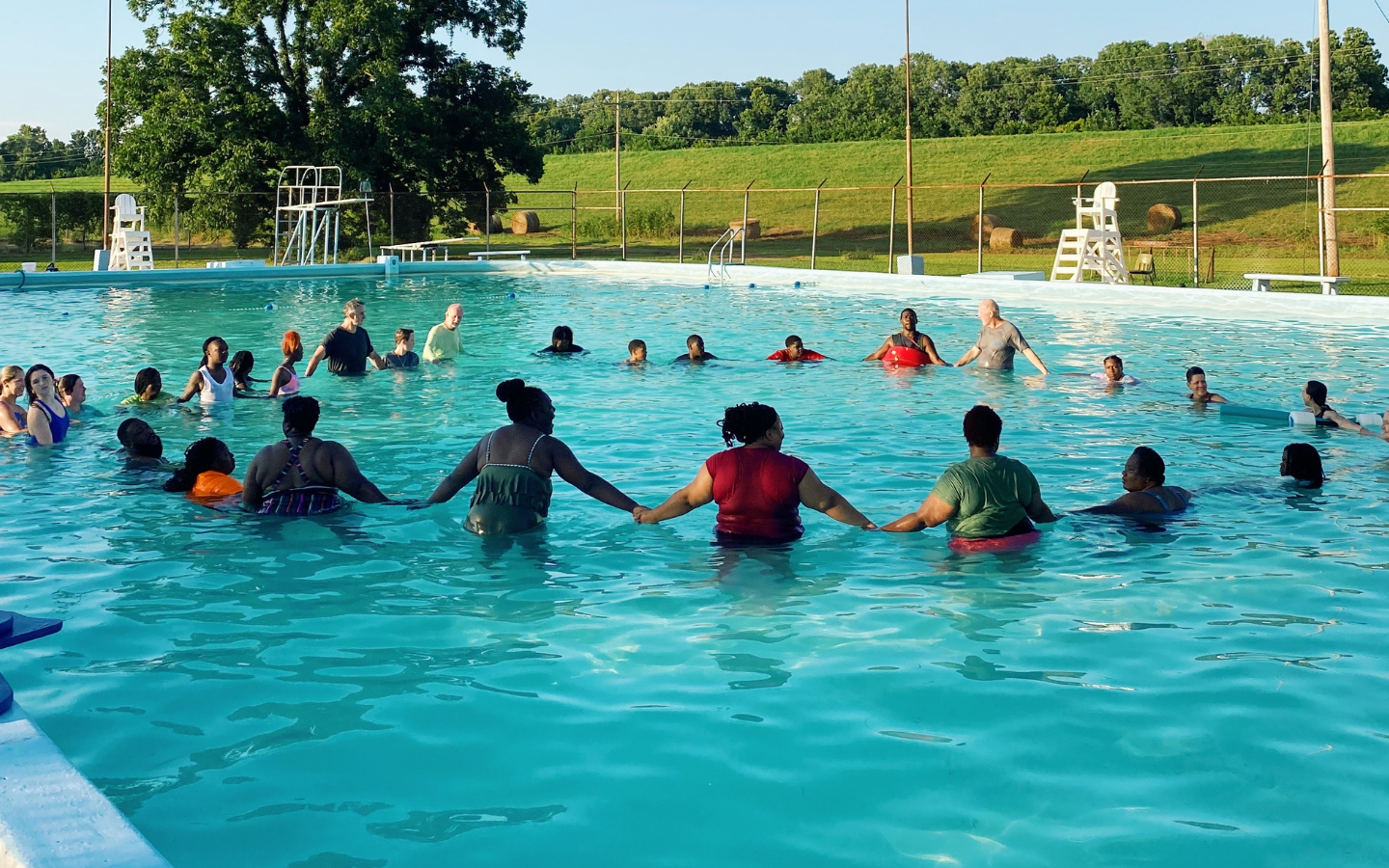 An image of participants of Together for Hope’s “Swim Camp” holding hands in a circle in a pool.