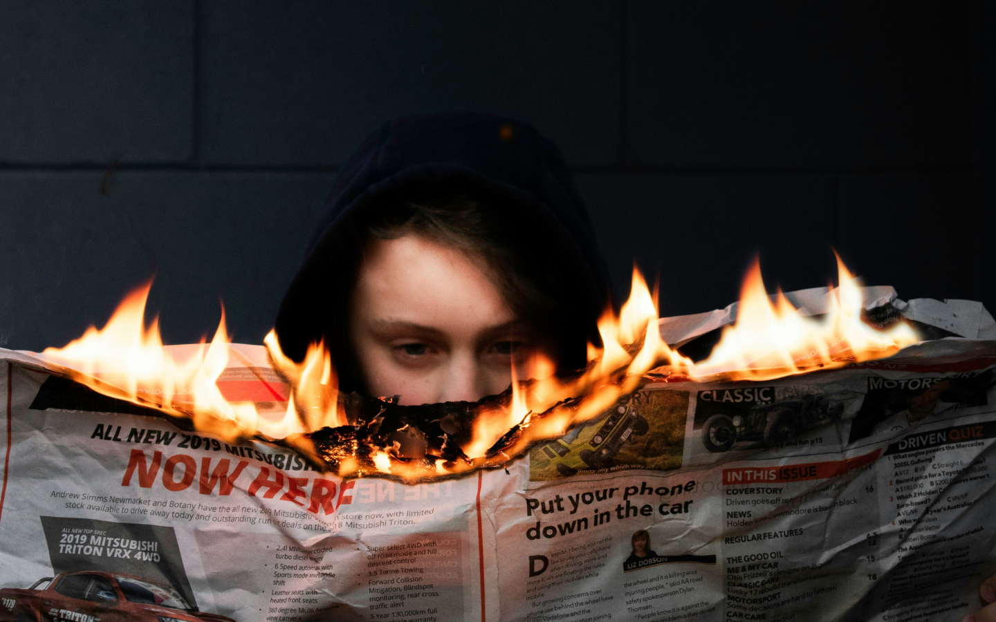 A woman holds and attempts to read a newspaper that is on fire.