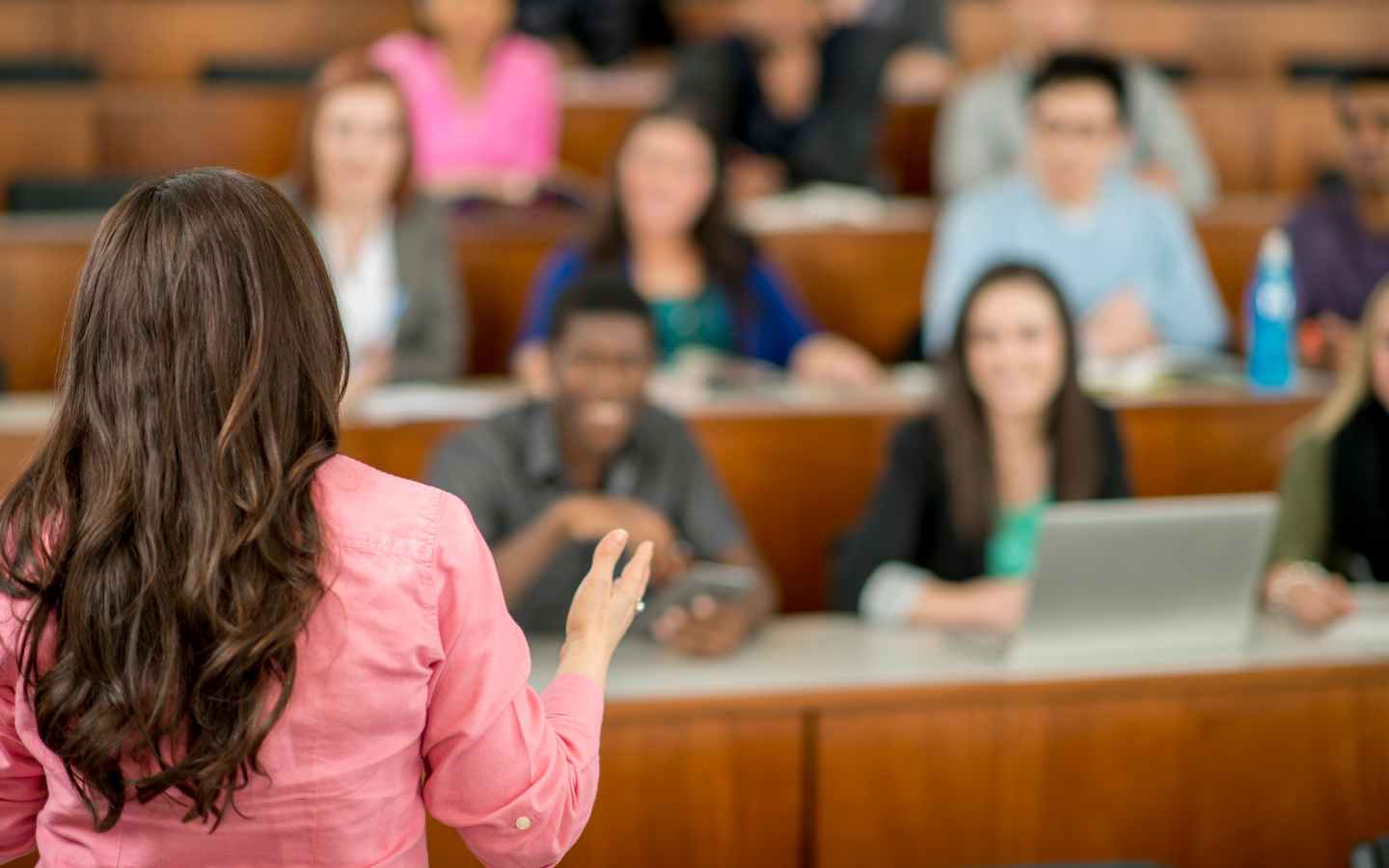 A female college professor teaches in a theater-style college classroom.