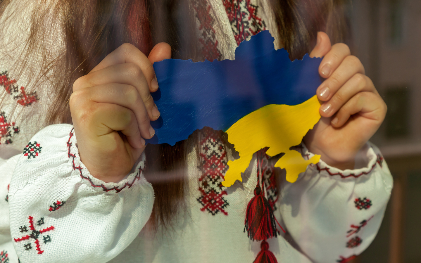 A Ukrainian girl in an embroidered dress holds a map of Ukraine painted in the colors of the Ukrainian flag.