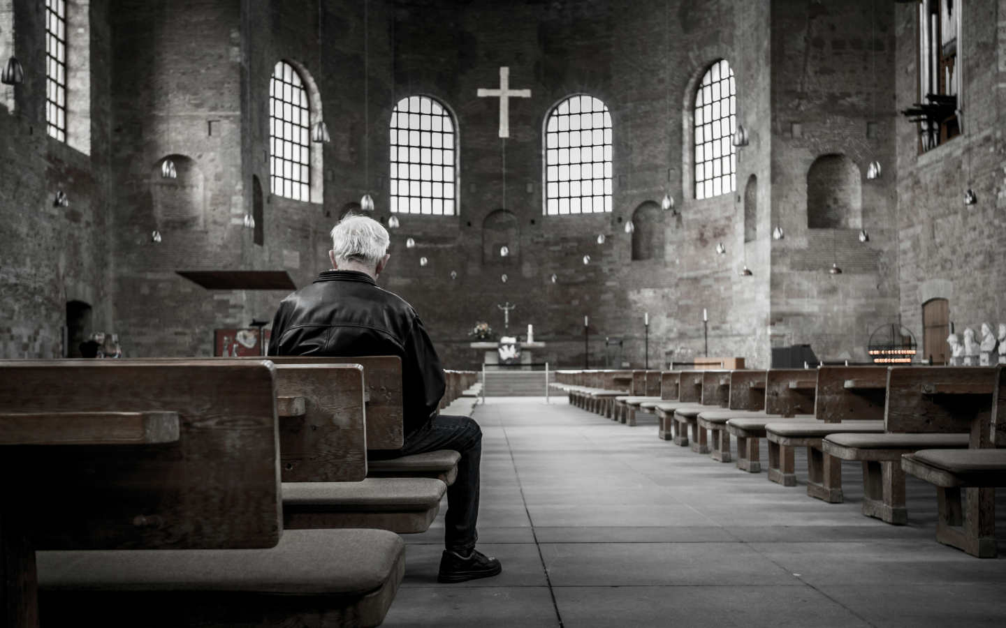 A elderly man sits alone in an old sanctuary.