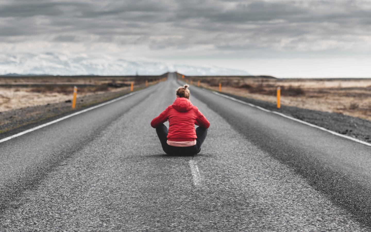 A woman sits in the middle of a road at the foot of mountains.