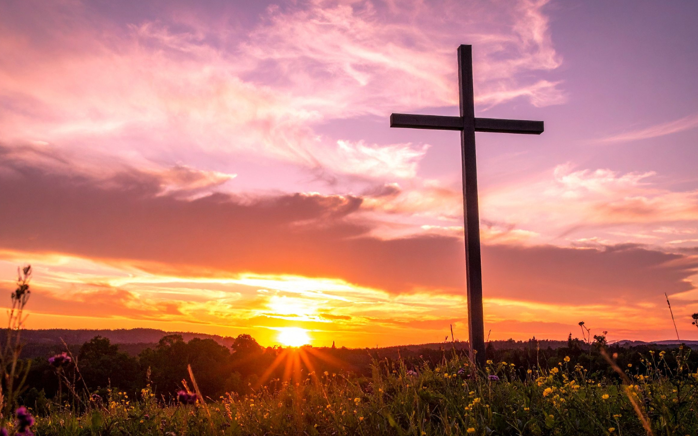 The silhouette of a cross in a colorful field at sunrise.