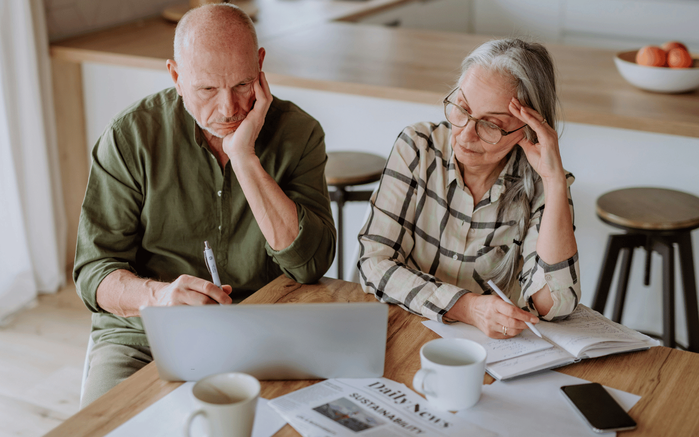 An elderly couples sits at a kitchen table working on paying bills.