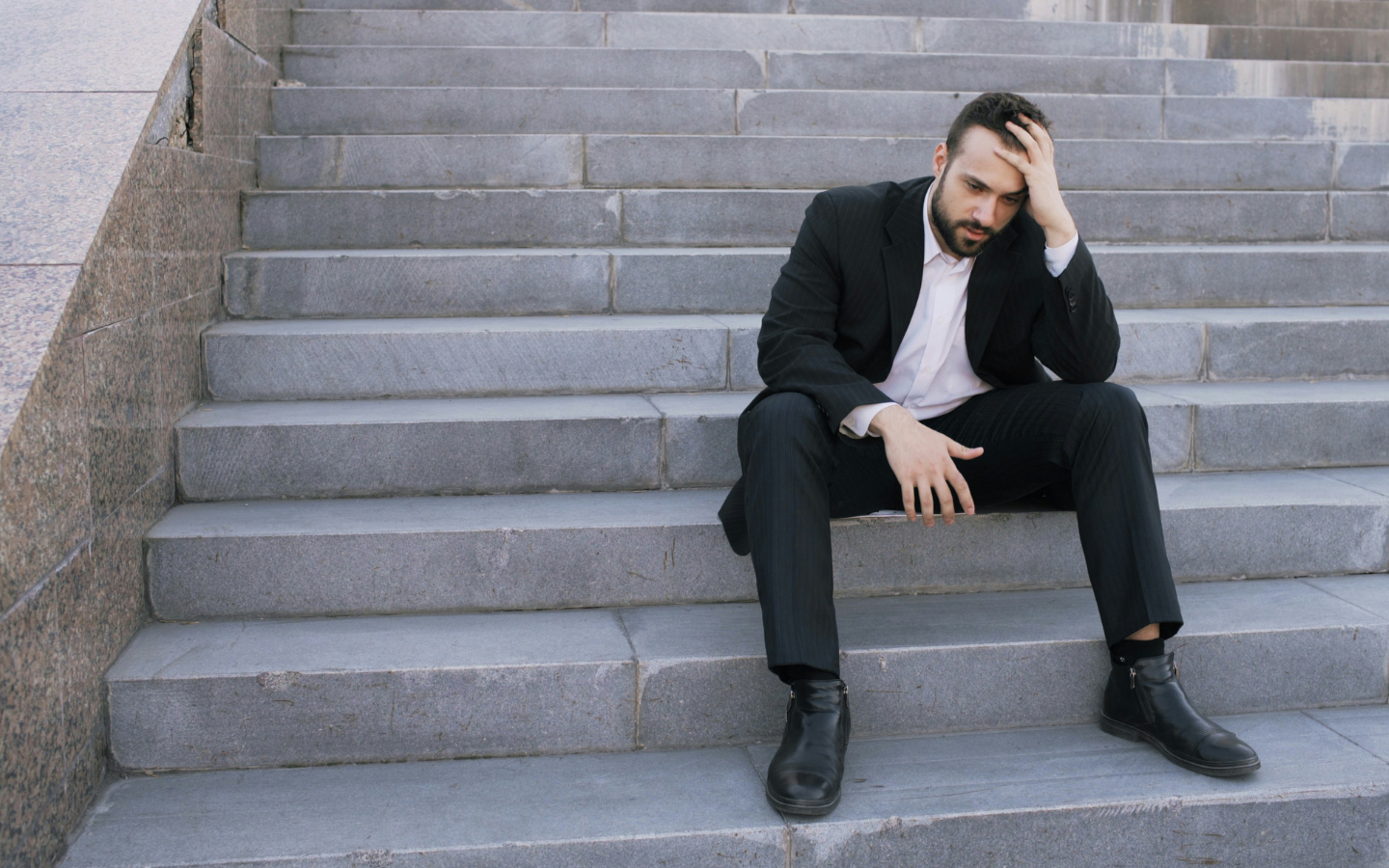 A man sits destitute on stone steps.
