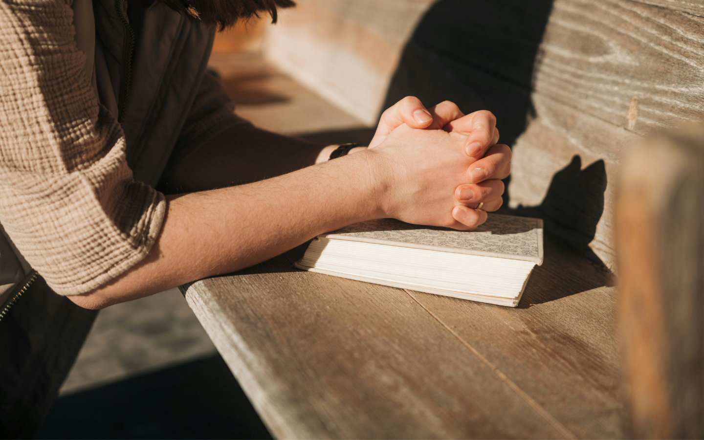 A person prays kneeling at a pew with a Bible.