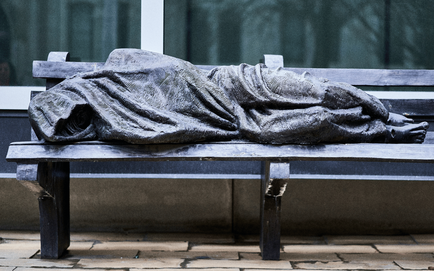 A statue of a homeless Jesus lying on a park bench.