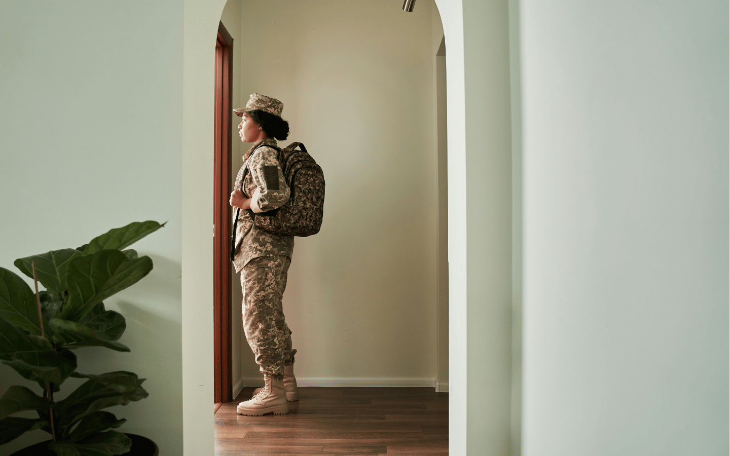 A soldier stands at the doorway of her home, preparing for deployment.