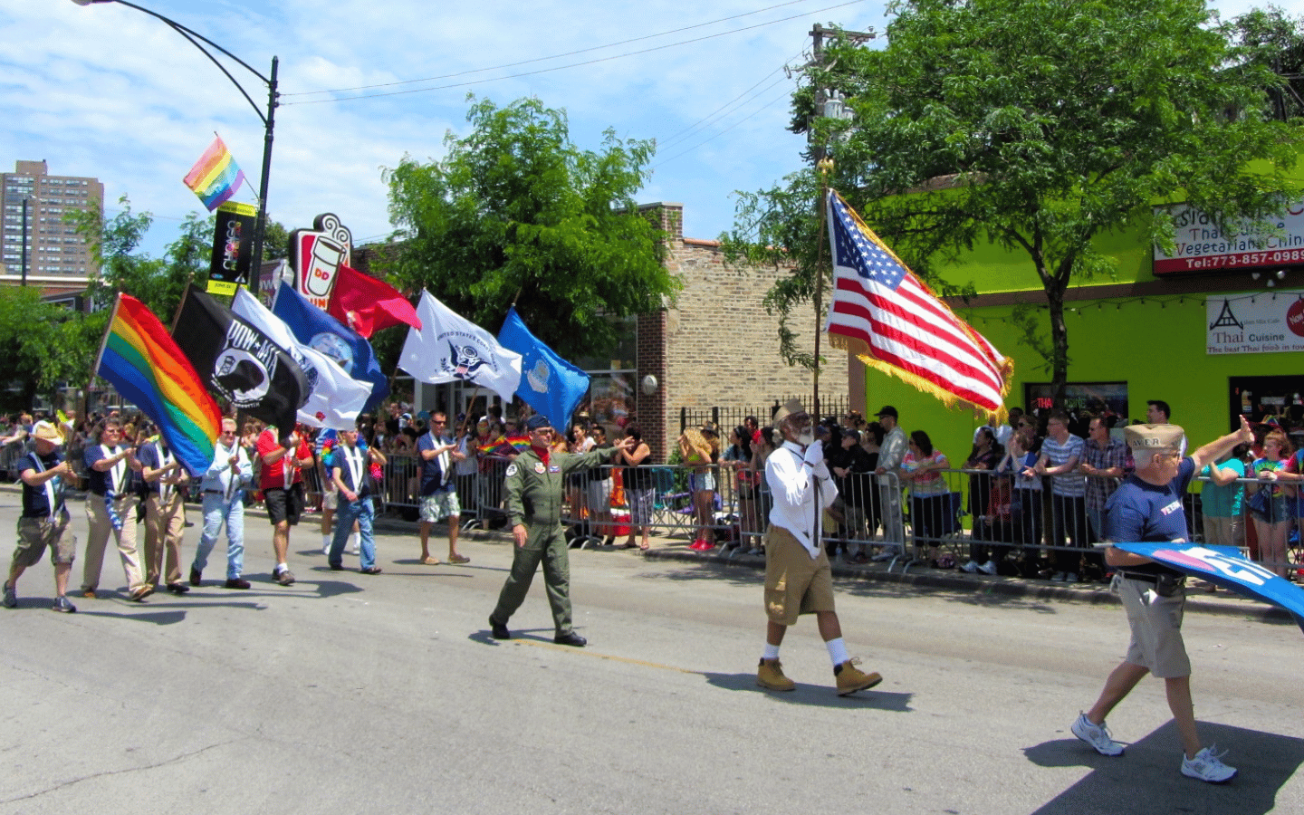 A veterans day parade with the Pride Flag alongside POW and service flags