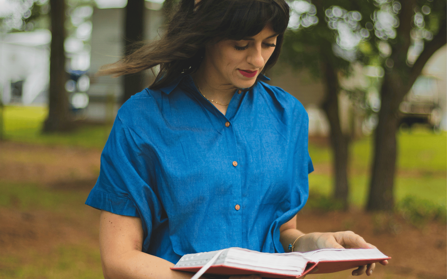 A woman reads a bible outside a church building.