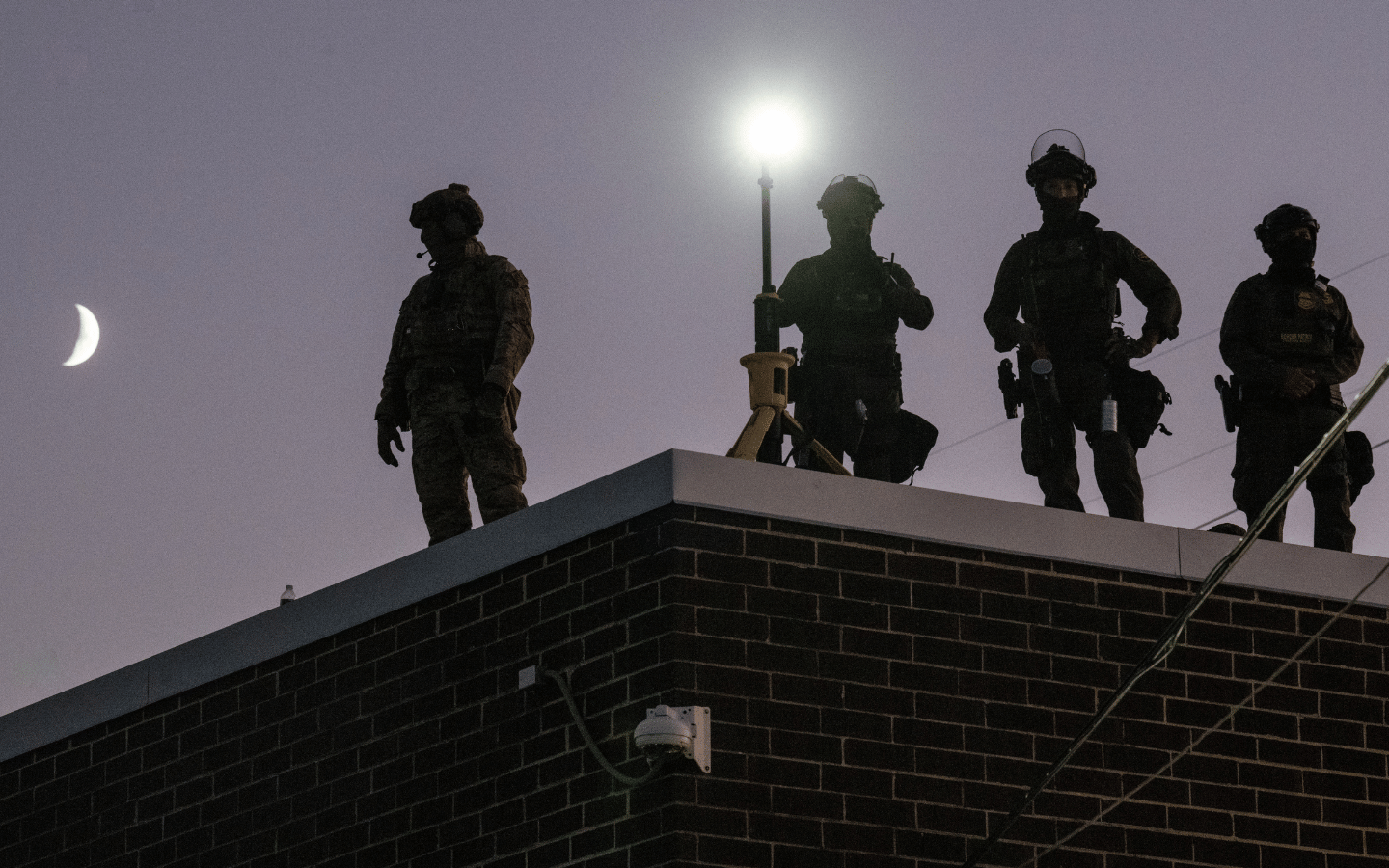 ICE agents stand guard over the Broadview detention center, with the moon and a star shining behind them.