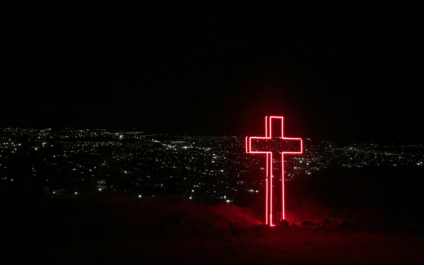 A large neon cross towers over a city at night.