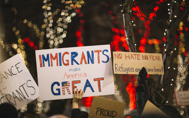 A crowd gathered and holding an assortment of signs in support of immigrants and refugees.