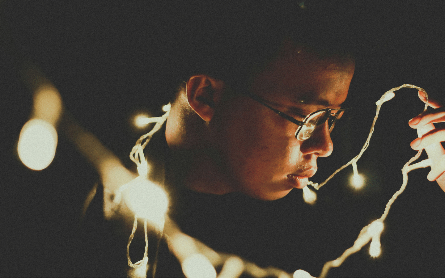 A man with a wistful look on his face fidgets with Christmas lights.