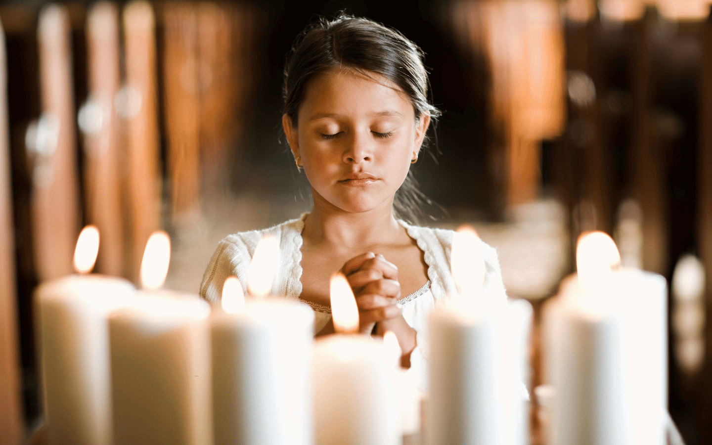 A young girl prays in front of a row of candles.