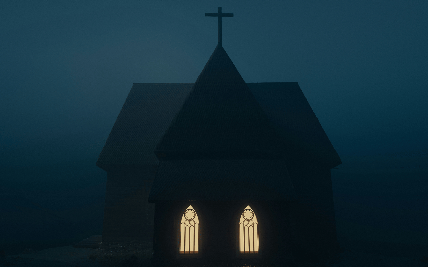 A church on a dark, foggy night with its window lit up from the inside.