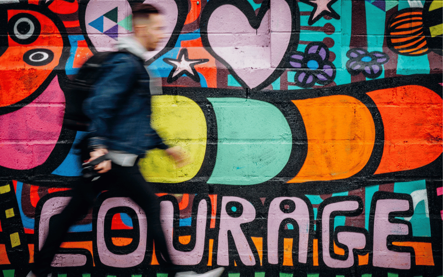 A blurred image of a man walking beside street art that reads “Courage.”