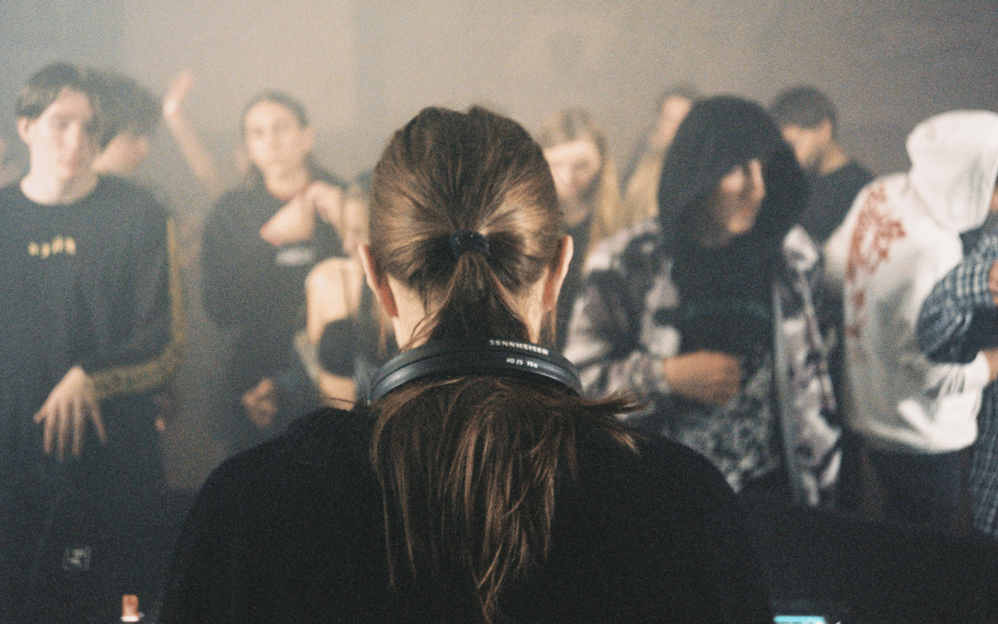 A woman in black stands confidently in a hazy, crowded room.
